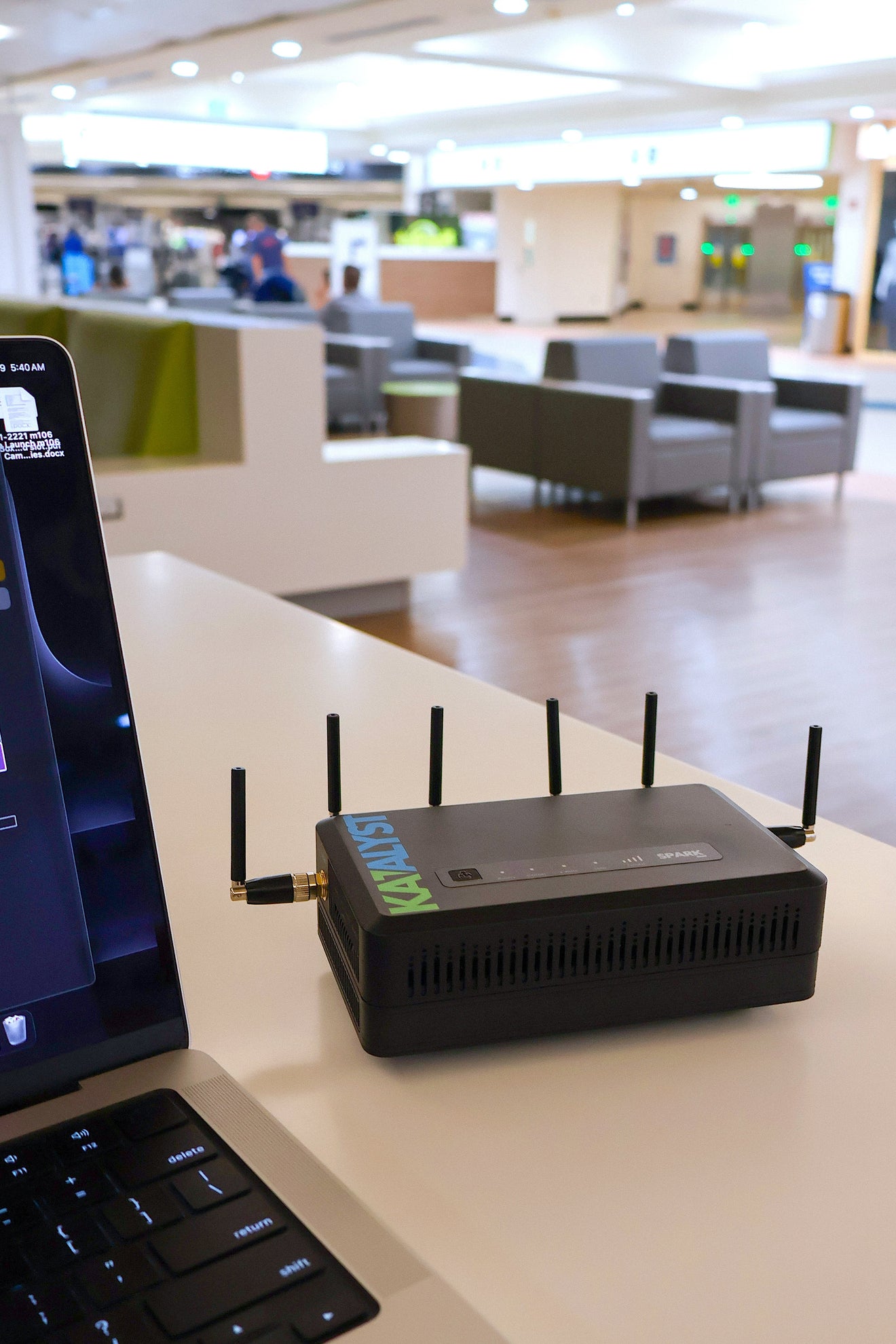 Katalyst Spark K500A portable 5G business router on a desk next to a laptop in an airport.