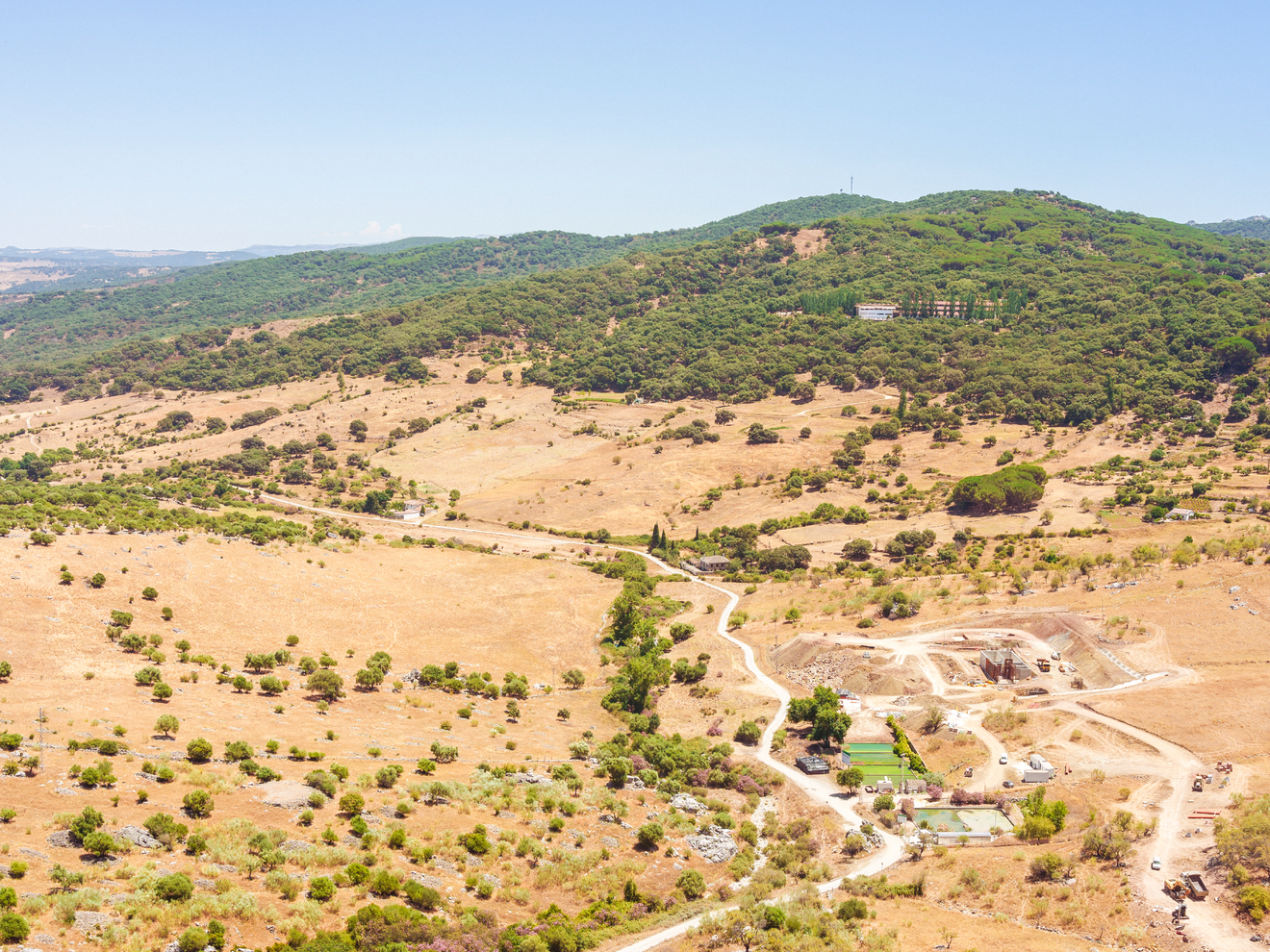 Aerial view of a rural landscape with rolling hills, open land, and scattered buildings.